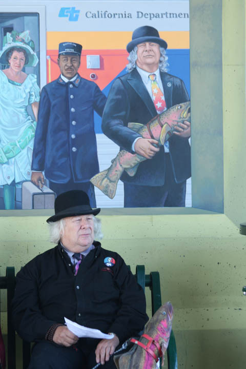 Photo of Wavy Gravy walking his fish in front of mural of Wavy Gravy Walking His Fish at the Berkeley Amtrak Railroad Station